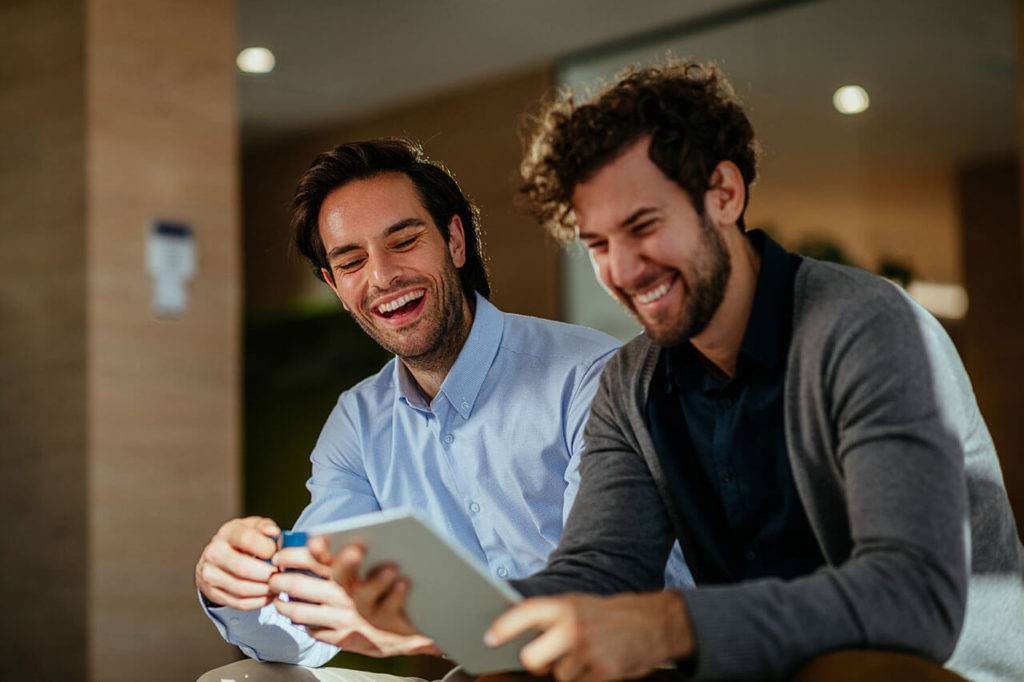 2 men laughing over an article they are reading on a tablet
